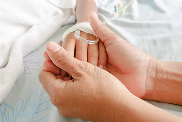 mother holding child\\'s hand who fever patients have IV tube.