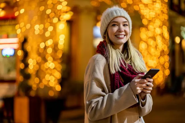 Portrait of beautiful young woman using her mobile phone in the street with christmas decoration on background