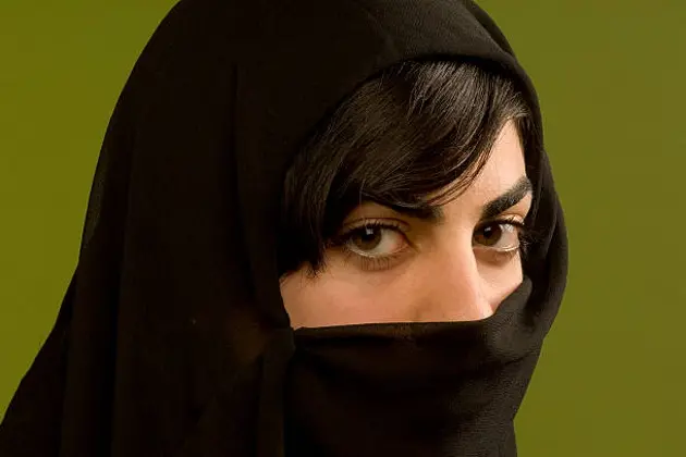 close up of a young woman wearing a veil looking at the camera on green background