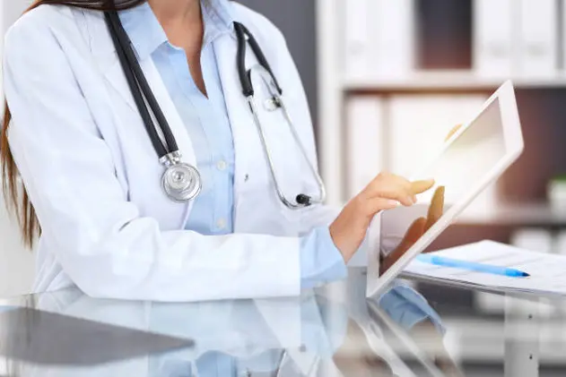 Close-up of female physician hands using digital tablet  while sitting at glass desk at hospital office. Medicine and healthcare concept.