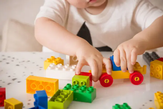 Close up of child\\'s hands playing with colorful plastic bricks at the table. Toddler having fun and building out of bright constructor bricks. Early learning.  stripe background. Developing toys