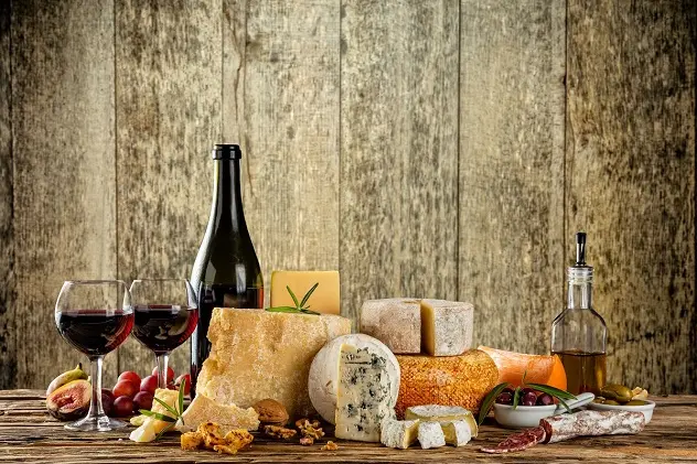 Various types of cheese, glasses and bottle of red wine placed on wooden table, copyspace for text. Wooden planks on background