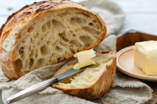 Sliced loaf of artisanal bread and butter knife on linen cloth close-up, selective focus.