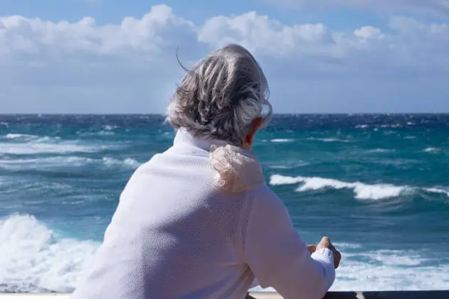 Back view of a senior woman with wind in the hair looking at the horizon over water. Active elderly retiree in winter holiday