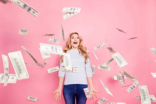 Omg, wow! Portrait of funny impressed girl with unexpected unbelievable reaction standing under shower from hundred 100 dollars, flying money isolated on pink background