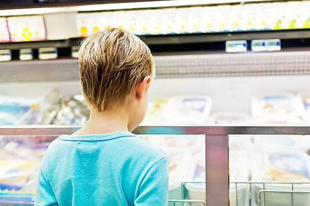 The backview of a cute little blonde girl looking longingly into the icecream fridge in a supermarket.