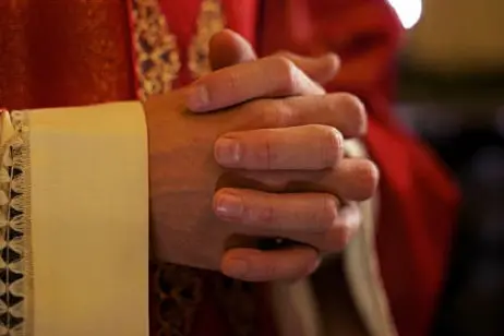 Catholic priest on altar praying with hands joined during mass service in church