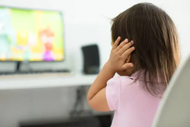 A child watching tv holding her ears because she is afraid of the sound; Child behavior theme