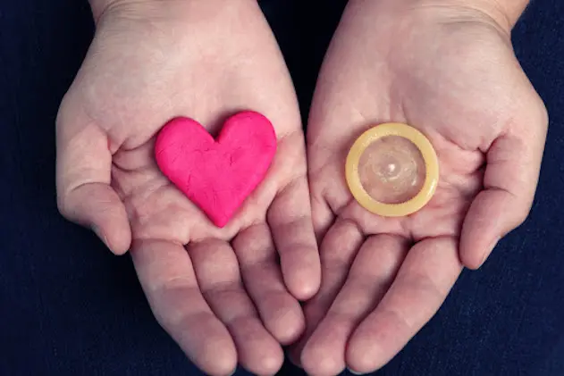 Woman\\'s hands hold a heart shape and a condom. Concept image.