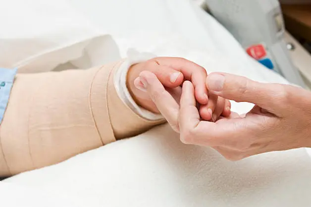 Hands of mother holding a 5 year old girl\\'s hand with bandage in hospital bed. (Focus is on hand.)