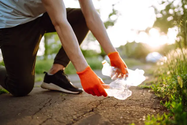 Men hand collects plastic trash for cleaning in the park. Volunteer wearing protective gloves collects bottle plastic. Environmental protection, ecological concept. Waste recycling.