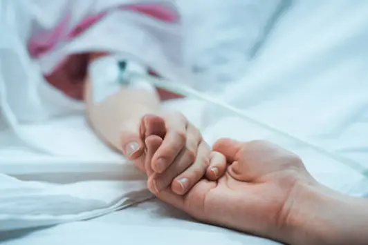 Recovering Little Child Lying in the Hospital Bed Sleeping, Mother Holds Her Hand Comforting. Focus on the Hands. Emotional Family Moment.