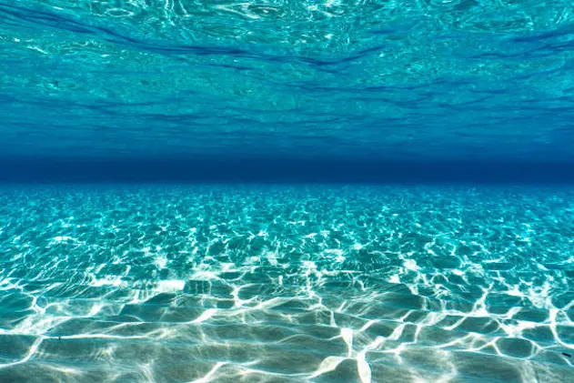 Crystal clear blue water, blue sky and white sand in the ocean floor, background