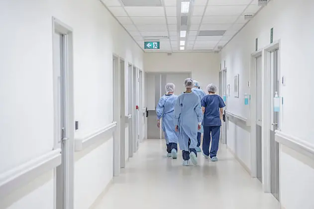 View from behind of four doctors in hospital corridor walking away from camera. Medical team in modern hospital corridor wearing surgical scrubs