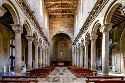 The majestic and imposing central nave and apse of the Duomo of San Lorenzo (Cathedral of Saint Lawrence), in the heart of the medieval city of Viterbo, in central Italy. Built in the Romanesque style in the 12th century, this cathedral became important in the history of the Catholicism when in the 13th century Viterbo became the seat of the Roman Pontiffs. The medieval center of Viterbo, the largest in Europe with countless historic buildings, churches and villages, stands on the route of the ancient Via Francigena (French Route) which in medieval times connected the regions of France to Rome, up to the commercial ports of Puglia, in southern Italy, to reach the Holy Land through the Mediterranean. Located 100 kilometers north of Rome along the current route of the Via Cassia and recognized as a city with a papal document from the year 852 AD, Viterbo is characterized by its stone and tuff constructions, materials abundantly present in this region of central Italy and which have always been used for the construction of houses and churches. Super wide angle image in high 16:9 and definition format.