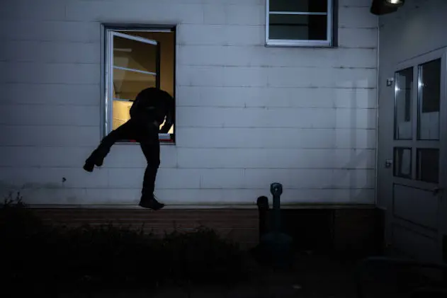 Rear View Of A Burglar Entering In A House Through A Window