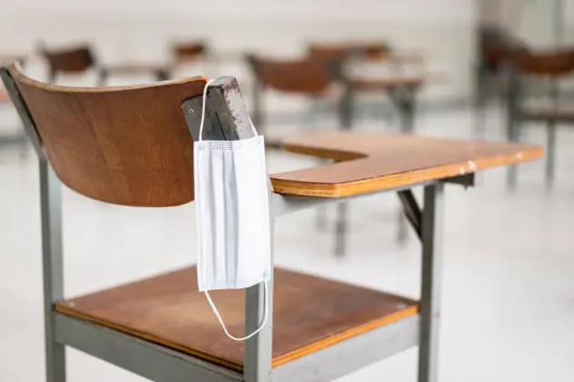 A used medical facemask hangs on a wood lecture chair in the empty classroom during the COVID-19 pandemic