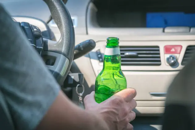 Man driving a car with a bottle of beer or other alcohol drink. Don\\'t drink and drive concept