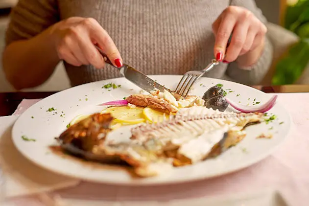 unrecognizable woman in restaurant eating fish,plate in front of her.