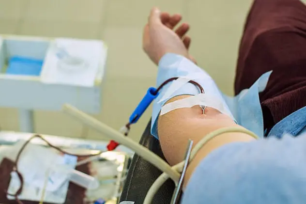 Image showing a young man\\'s hand with a needle for blood collection in it for blood donation as he is lying in a special chair in a hospital.