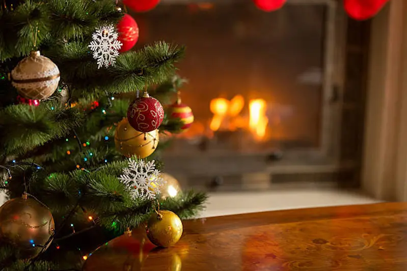 Closeup image of golden and red baubles on Christmas tree in front of burning fireplace. Beautiful Christmas background