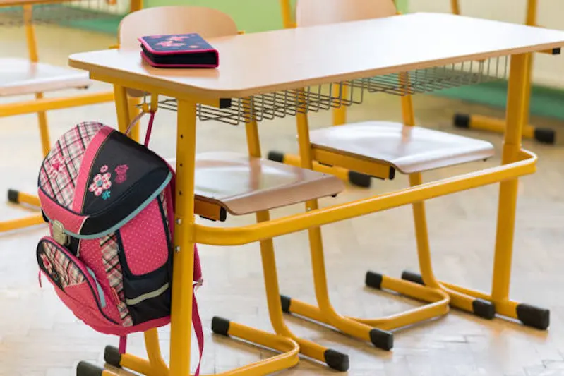 Pink girly school bag and pencil case on a desk in an empty classroom. First day of school concept.