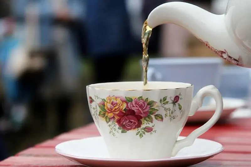 Tea being poured from floral patterned teapot into a bone china cup