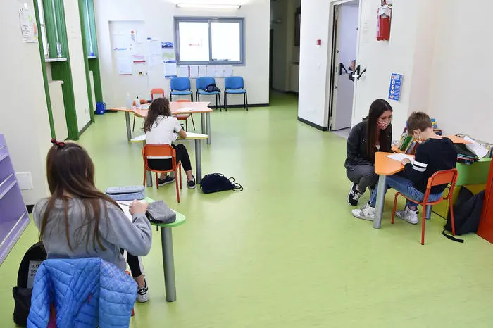 Un\\' educatrice parla con uno dei bambini delle elementari in una delle tre classi da 4-5 bimbi ciascuna per le elementari, due per i bimbi della materna, allestiti  nella palestra e nella ludoteca di Borgosesia di propriet\\u00E0 del Comune, Borgosesia, 12 Maggio 2020. Il servizio di assistenza per bambini da 3 a 10 anni, ideato dal Comune di Borgosesia e da quello di Quarona, \\u00E8 dedicato ai genitori che lavorano e non hanno altre soluzioni per accudire i figli. Controlli della temperatura all\\'ingresso, banchi distanziatati e zainetto in spalla, i bambini sono affidati a educatori professionali sottoposti a test sierologico, in ambienti sanificati e con accorgimenti che hanno avuto il via libera dall\\'Unit\\u00E0 di Crisi della Regione Piemonte. ANSA/ ALESSANDRO DI MARCO