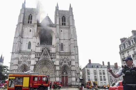 A French Police officer gestures as firefighters are at work to put out a fire at the Saint-Pierre-et-Saint-Paul cathedral in Nantes, western France, on July 18, 2020. - The major fire that broke out on July 18, 2020 inside the cathedral in the western French city of Nantes has now been contained, emergency services said. \"It is a major fire,\" the emergency operations centre said, adding that crews were alerted just before 08:00 am (0600 GMT) and that 60 firefighters had been dispatched. (Photo by Sebastien SALOM-GOMIS / AFP)