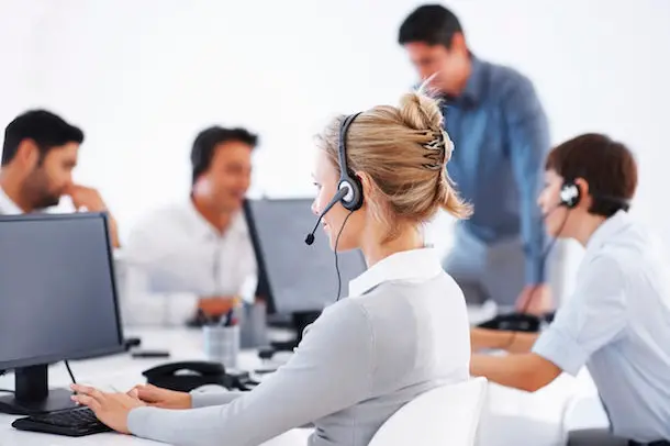 Business woman wearing headset working on computer with colleagues in background