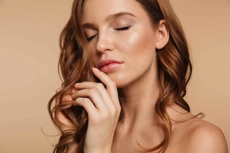 Close up Beauty portrait of sensual ginger woman with long hair posing with closed eyes over cream background