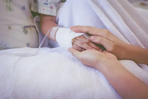 Close up hand of parent holding hand of child in hospital, saline intravenous (IV) on hand, shallow depth of field (DOF) saline intravenous (IV) in focus. Vintage picture style.