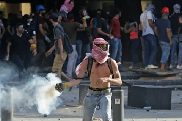 A Lebanese protester throws a tear-gas canister back at security forces in downtown Beirut on August 8, 2020, following a demonstration against a political leadership they blame for a monster explosion that killed more than 150 people and disfigured the capital Beirut. (Photo by JOSEPH EID / AFP)