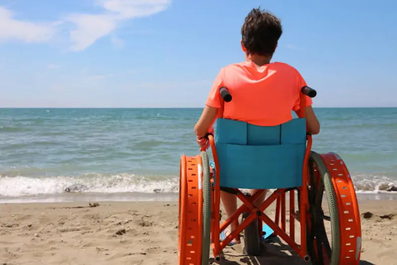 boy on the special wheelchair with metal wheels on the beach by the sea