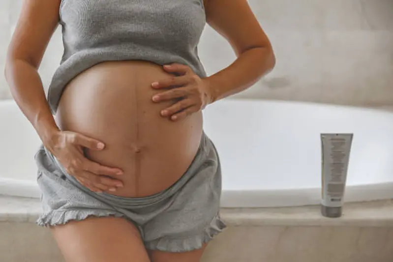 Close-up front view shot of unrecognizable pregnant Indonesian woman rubbing her big belly after applying a stretch mark cream