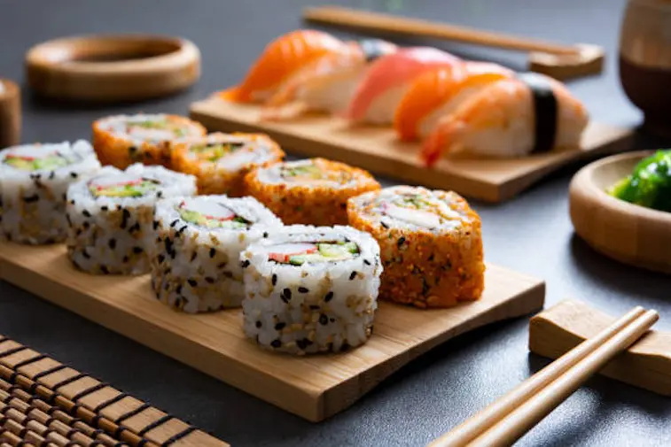 Sushi set uramaki and spicy sushi rolls served on bamboo tray. Various kinds of sushi pieces served on black slate with wooden chopstick. Japanese traditional food with bamboo service.