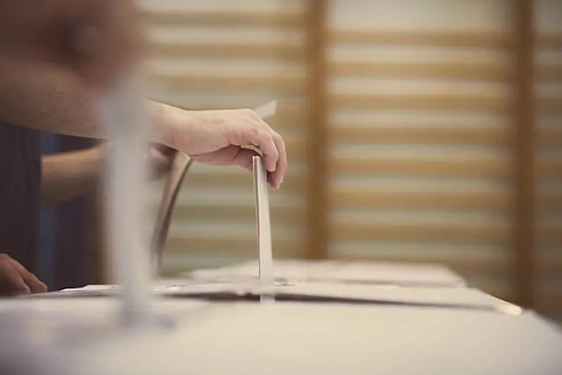 Hand of a person casting a ballot at a polling station during voting.