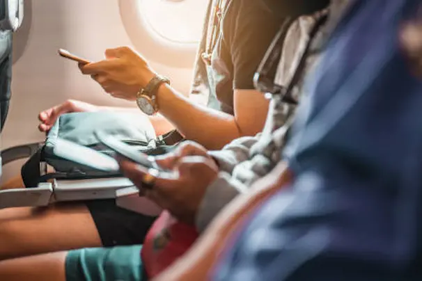 The tourists who are playing the phone and have a ticket on hand on the plane that is preparing to take-off. Airplane, Travel, Smartphone, Airport, ticket, technology concept.