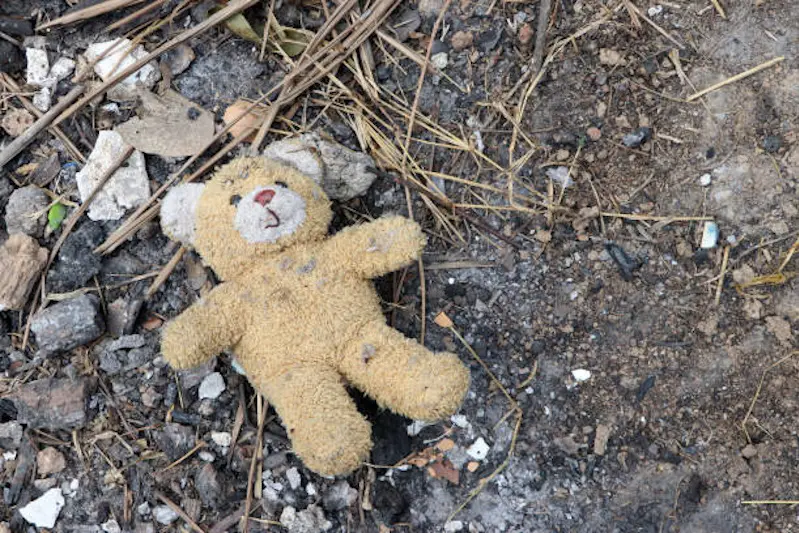 Old dirty teddy bear neglected on the ground soil. End of childhood.