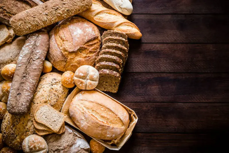 Top view of breads assortment like brunch bread, rolls, wheat bread, rye bread, sliced bread, wholemeal toast, spelt bread and kamut bread on dark brown rustic wooden table. Breads are at the left side of the image leaving a useful copy space at the right side on the table. Low key DSLR photo taken with Canon EOS 6D Mark II and Canon EF 24-105 mm f/4L