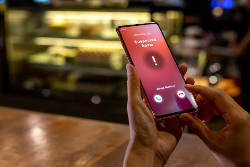 A woman receiving an incoming suspected spam call on her phone. The network provider detect the scam and show warning sign, woman rejects the call.