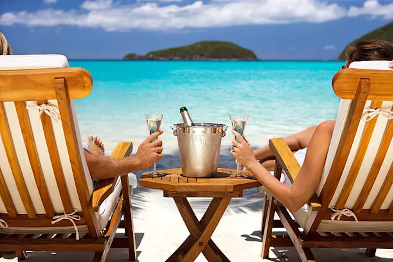 honeymoon couple sitting in luxury recliners at a tropical Caribbean beach resort and celebrating with a champagne