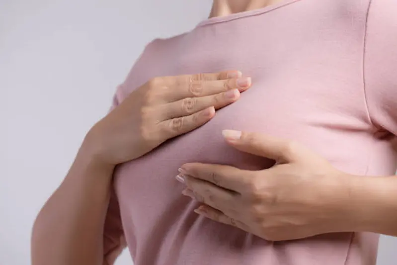 Woman hand checking lumps on her breast for signs of breast cancer on gray background. Healthcare concept.