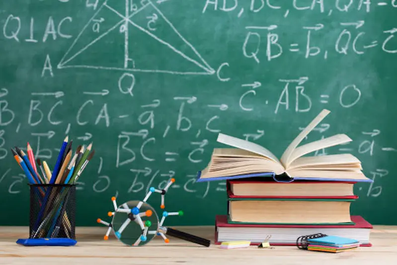 Education and sciences concept - books on the teacher desk in the auditorium, chalkboard on the background.