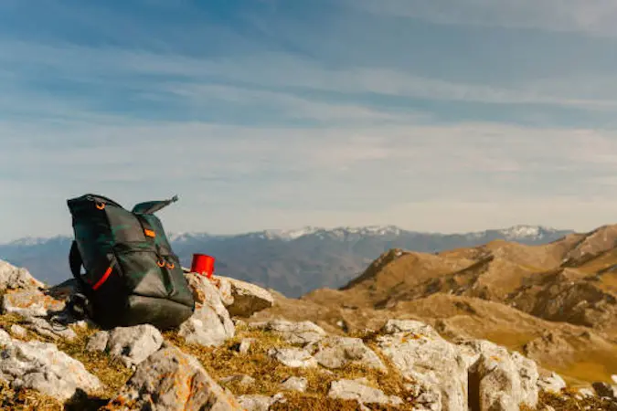 backpack photographer and hiker with red cup leaning on the rock of a mountain peak. adventure and sport concept. mountain landscape. mountain range. 16:9 format.