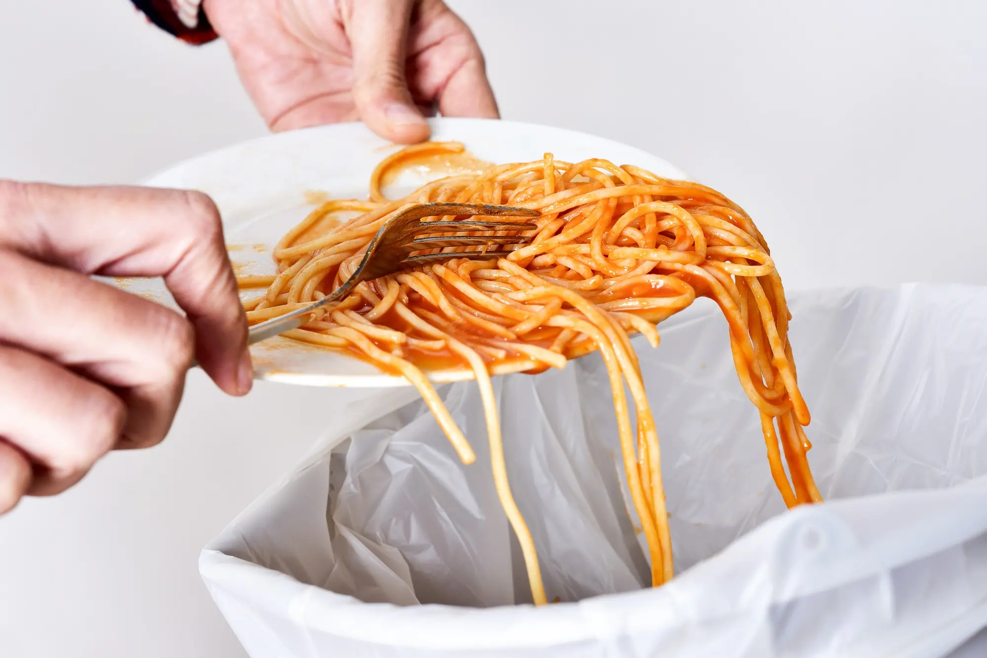 <p>closeup of a young man throwing the leftover of a plate of spaghetti to the trash bin</p>\\n